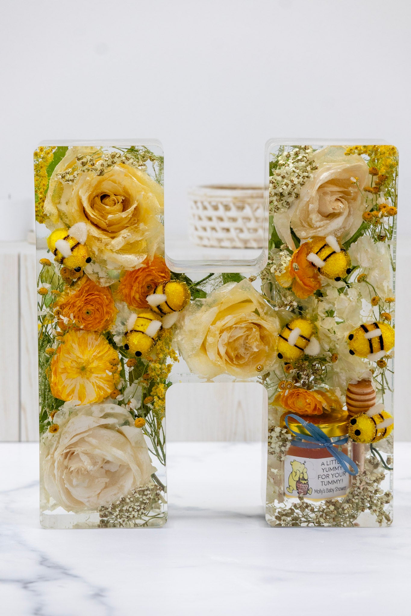 baby shower flower preservation letter 'H' made of preserved flowers, baby bees and honey jar favor on a white background