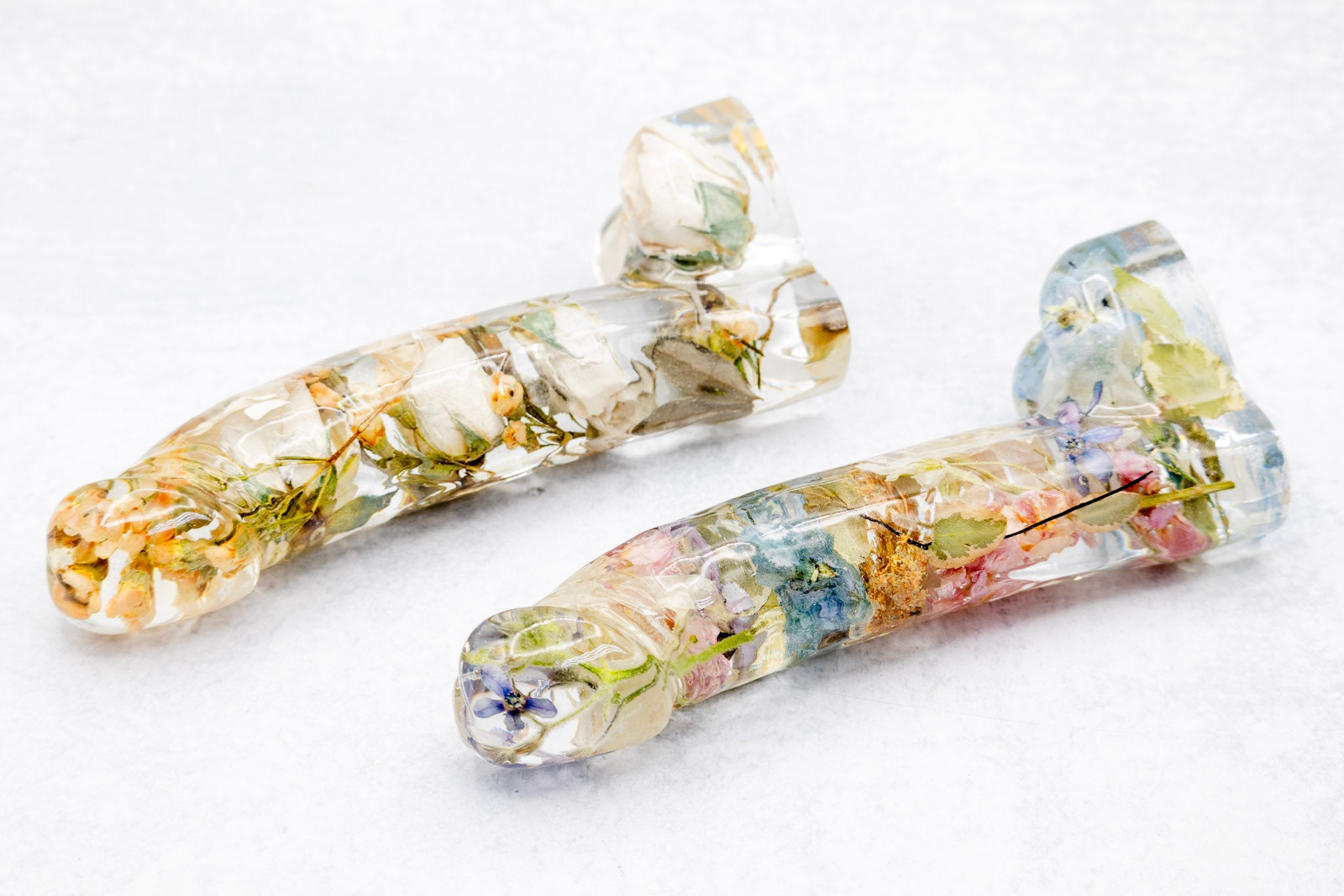 Two resin dildos, one with white flower color correction, the other with colorful preserved flowers