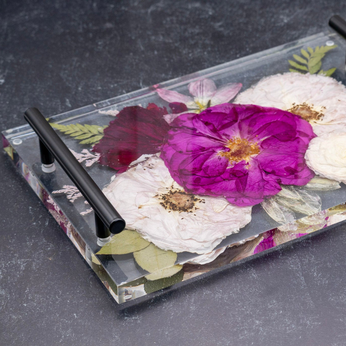 Decorative epoxy tray with pressed sentimental flowers encased and black handles on a dark surface