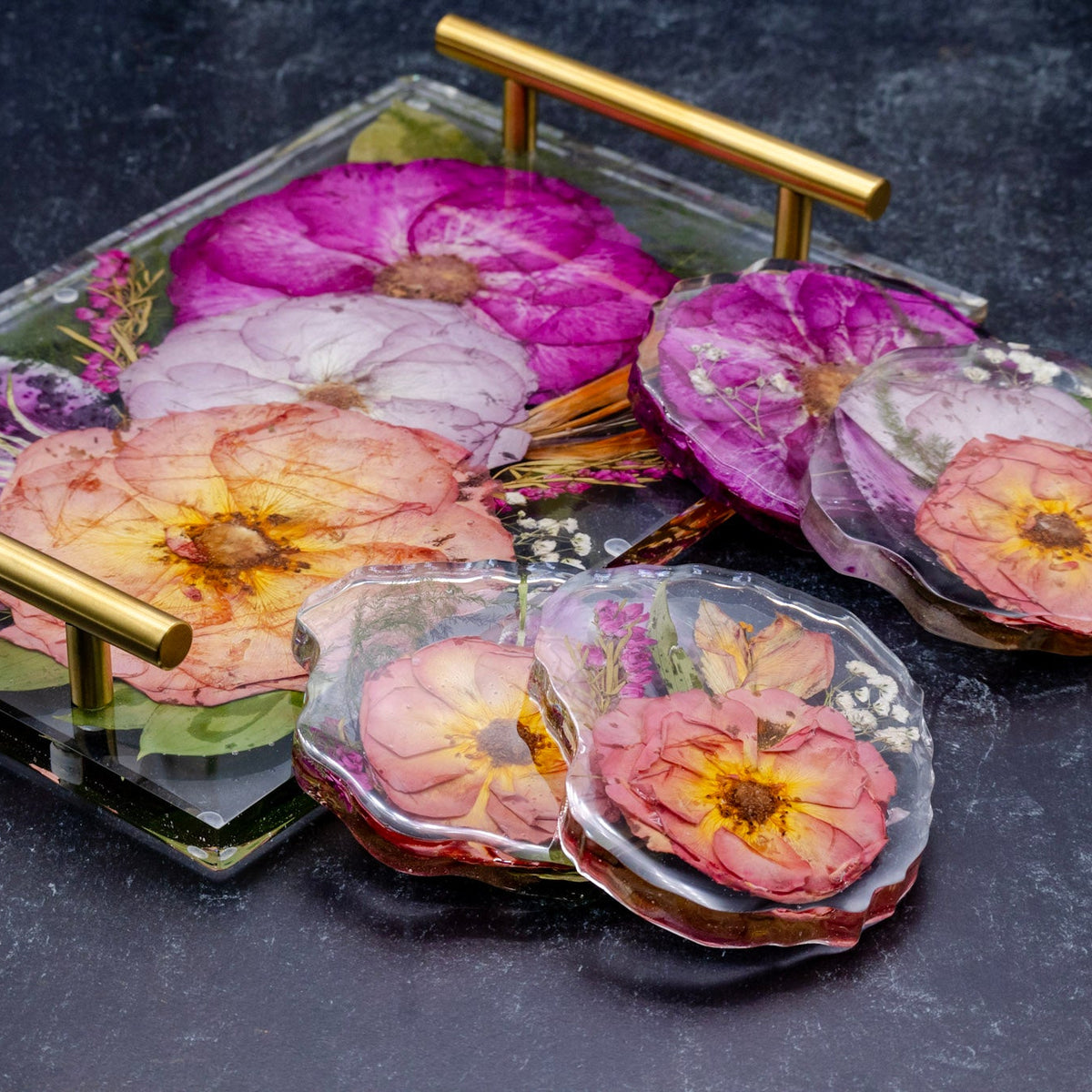 Tropical bouquet preservation encased in resin tray and pressed flower coaster set with gold handles on a dark surface