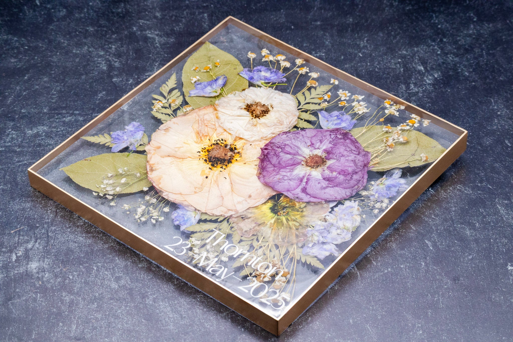 Decorative tray with pressed flowers and a personalized message on a dark surface