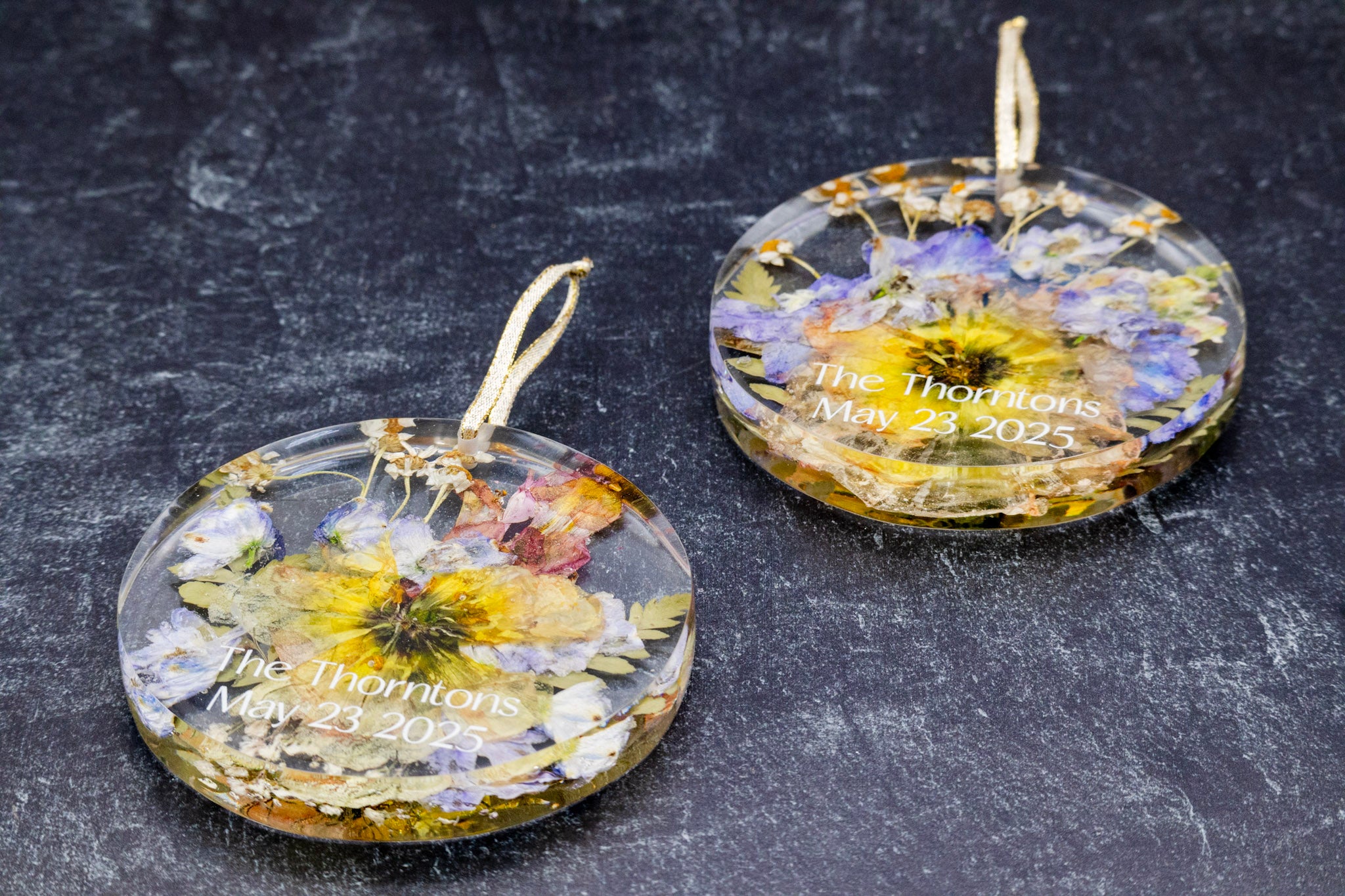 Two round glass ornaments with floral designs and engraved text on a dark surface