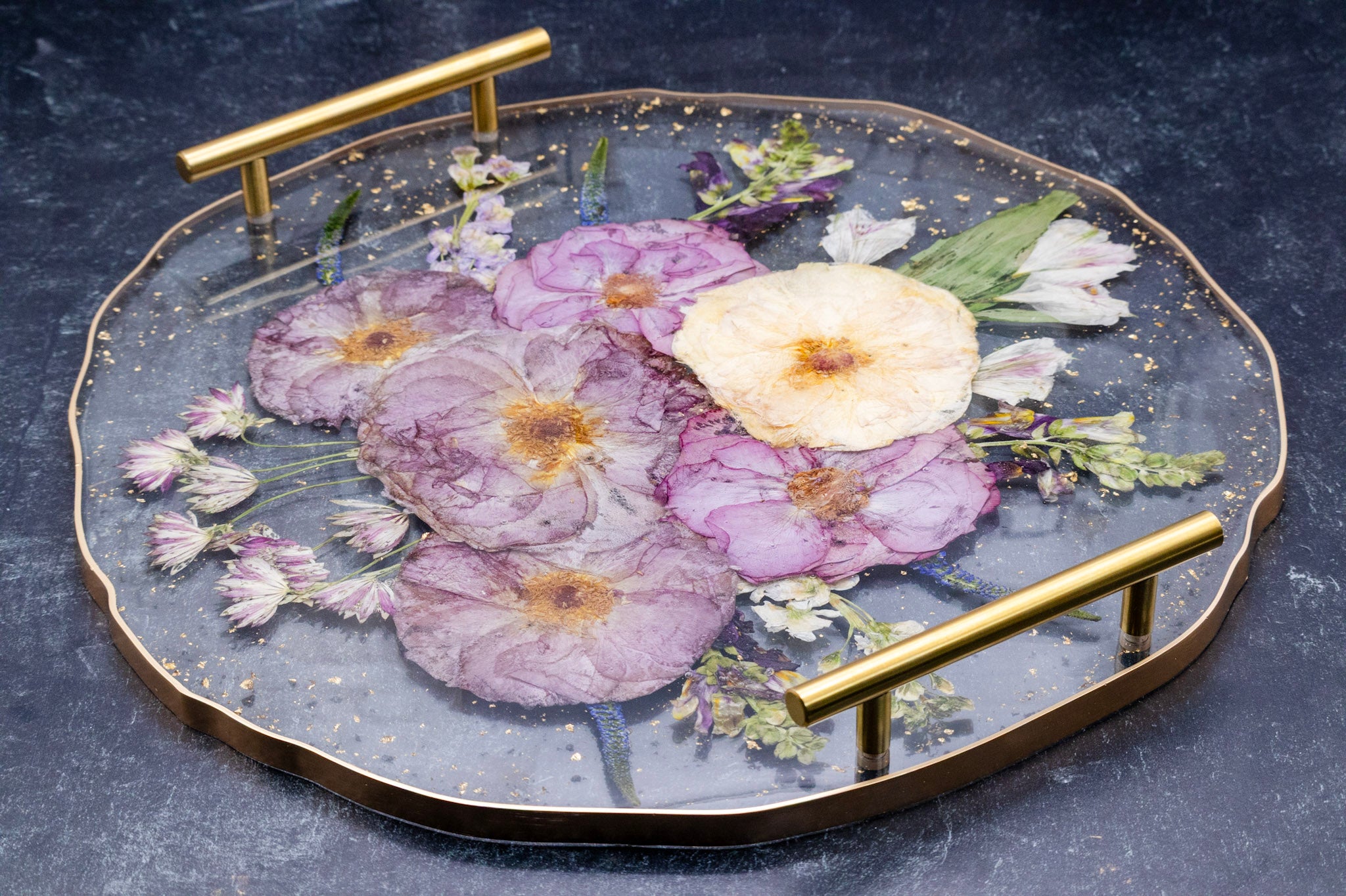epoxy resin tray with pressed floral design and gold handles on a dark background