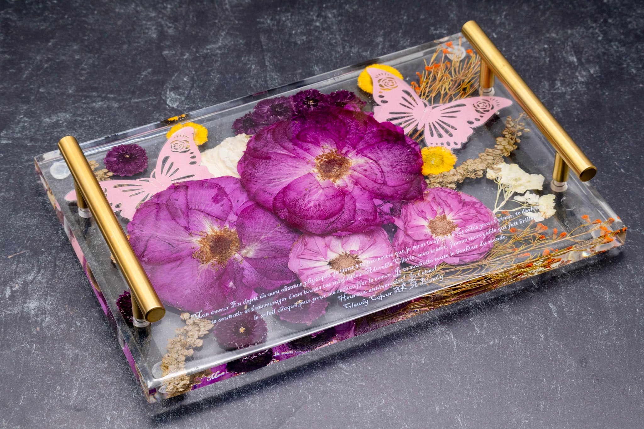 Decorative tray with pressed flowers and butterflies on a dark surface