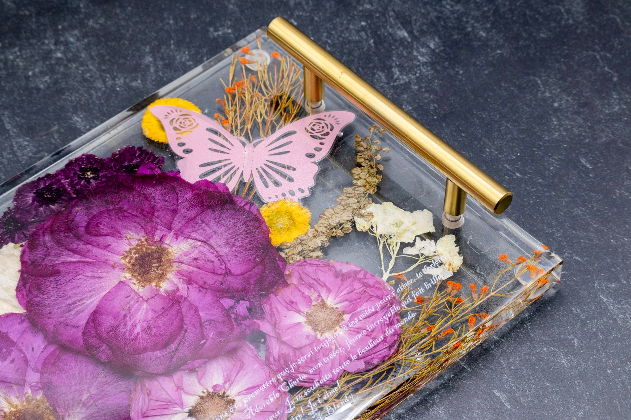 Decorative tray with flowers, butterflies, and a gold handle on a dark background