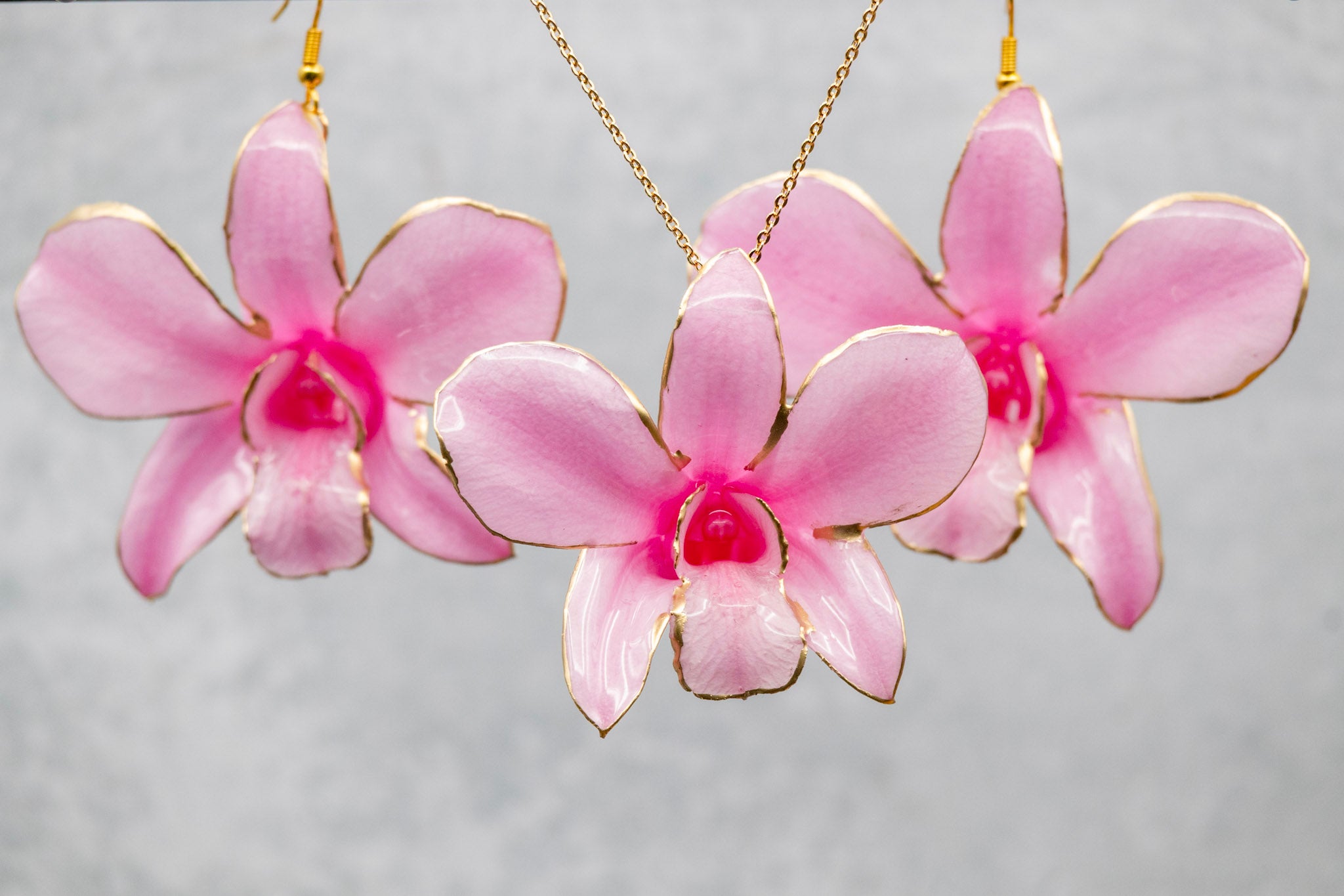 Pink orchid earrings with gold accents on a gray background