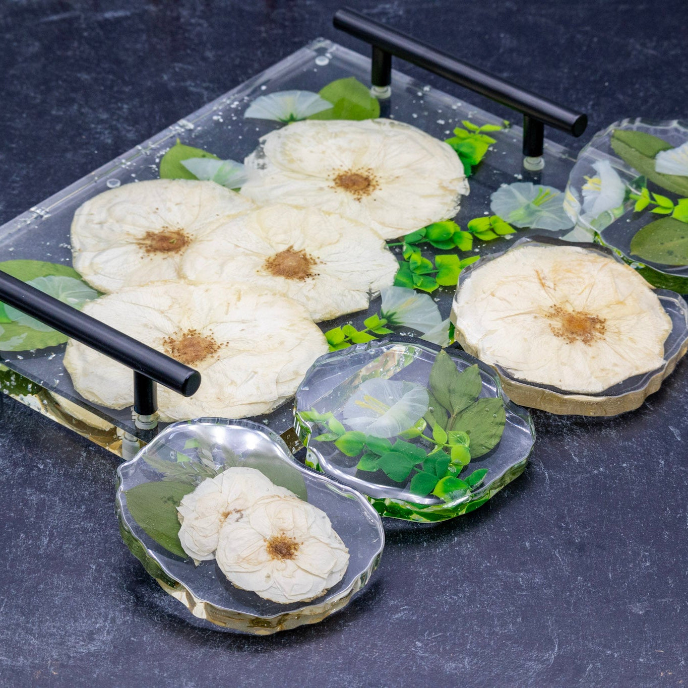 Pressed white rose bouquet preservation in resin serving tray with artificial greenery encased in resin geode coasters on a dark background