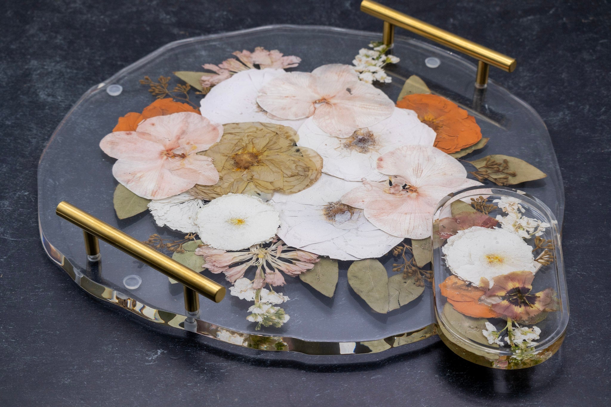 Landscape photo of a pressed flower 16-inch round resin tray with oval trinket tray on a dark surface