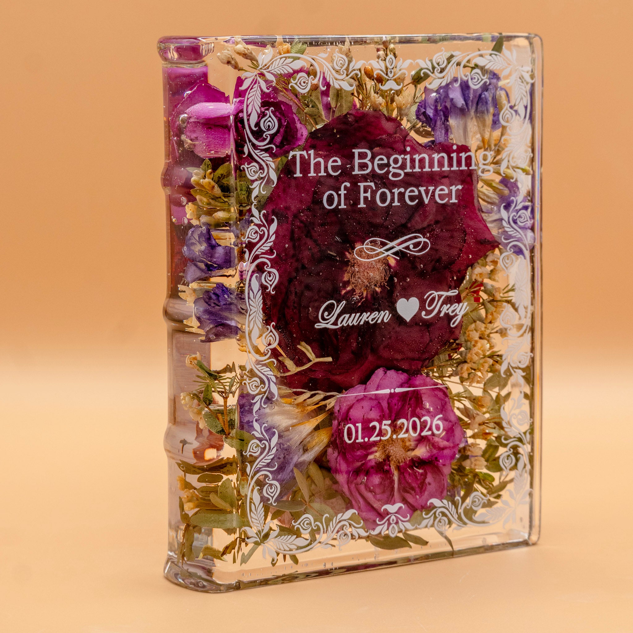 Book-shaped resin keepsake with preserved burgundy and pink roses and purple blooms, personalized with a couple's names and wedding date.