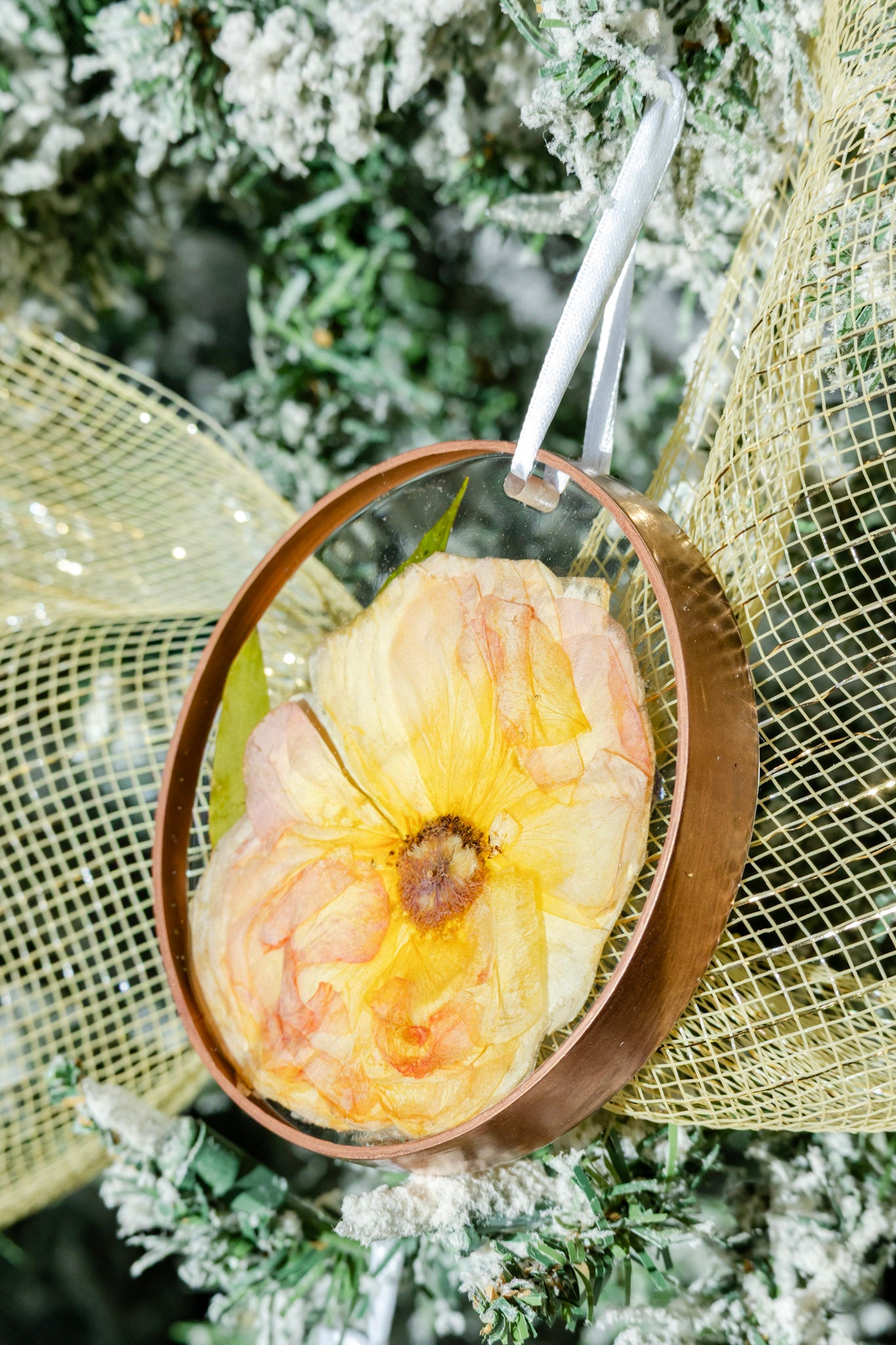 Decorative pressed flower ornament with a painted gold trim hanging on a Christmas tree. Wedding Flower Preservation keepsake