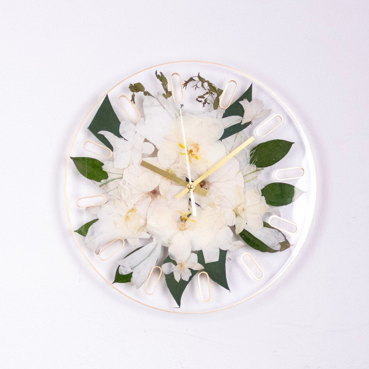 White orchid bouquet preservation in a resin wall clock with gold hands and gold painted trim on a white wall