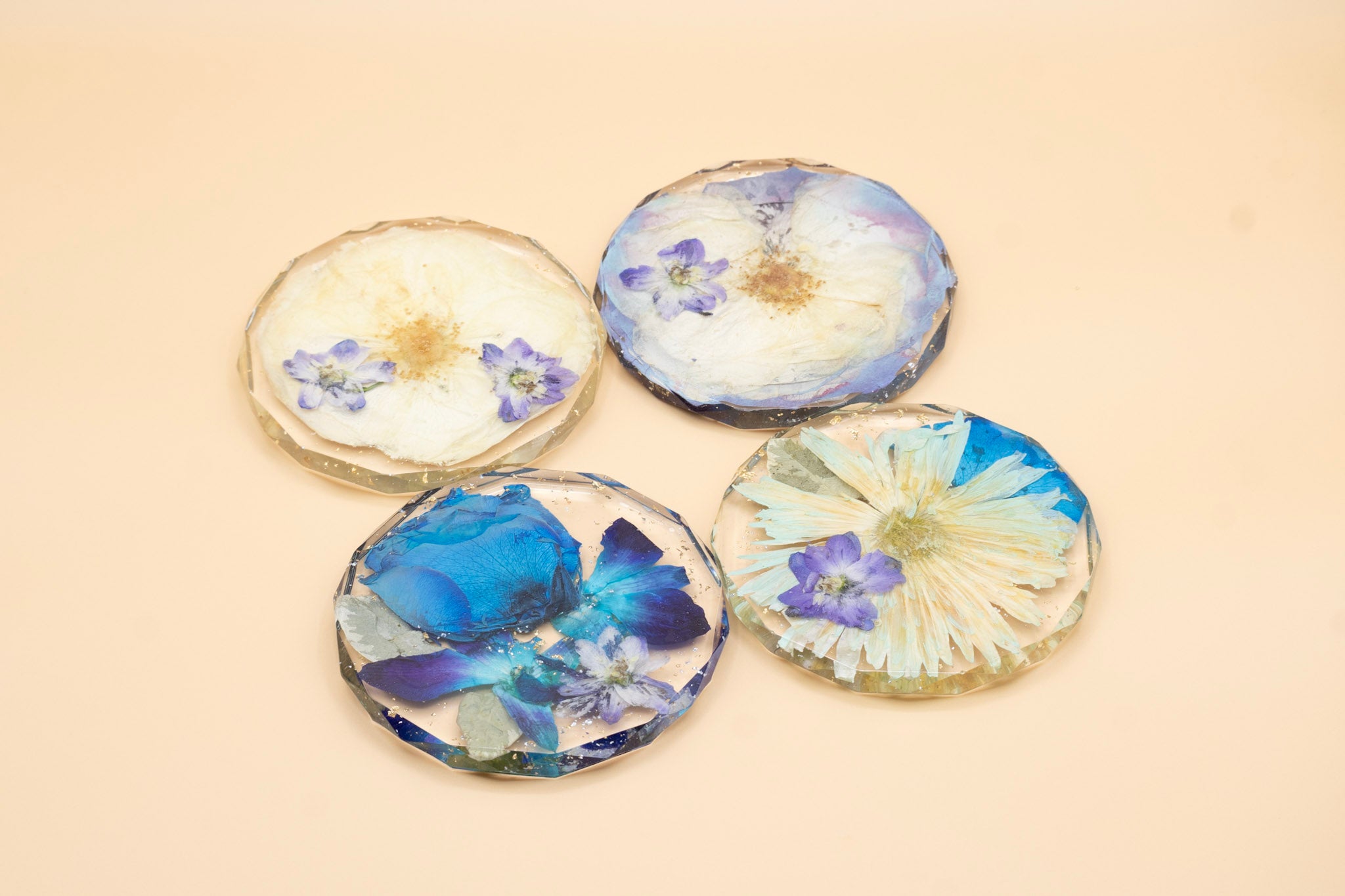 Four diamond coasters made with pressed flowers on a beige background