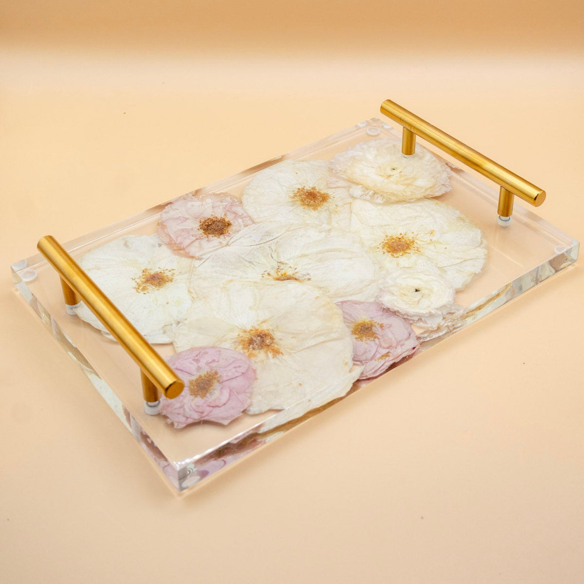 Resin flower preservation serving tray with gold metal handles, filled with dried white and pink pressed roses, set against a solid beige background.