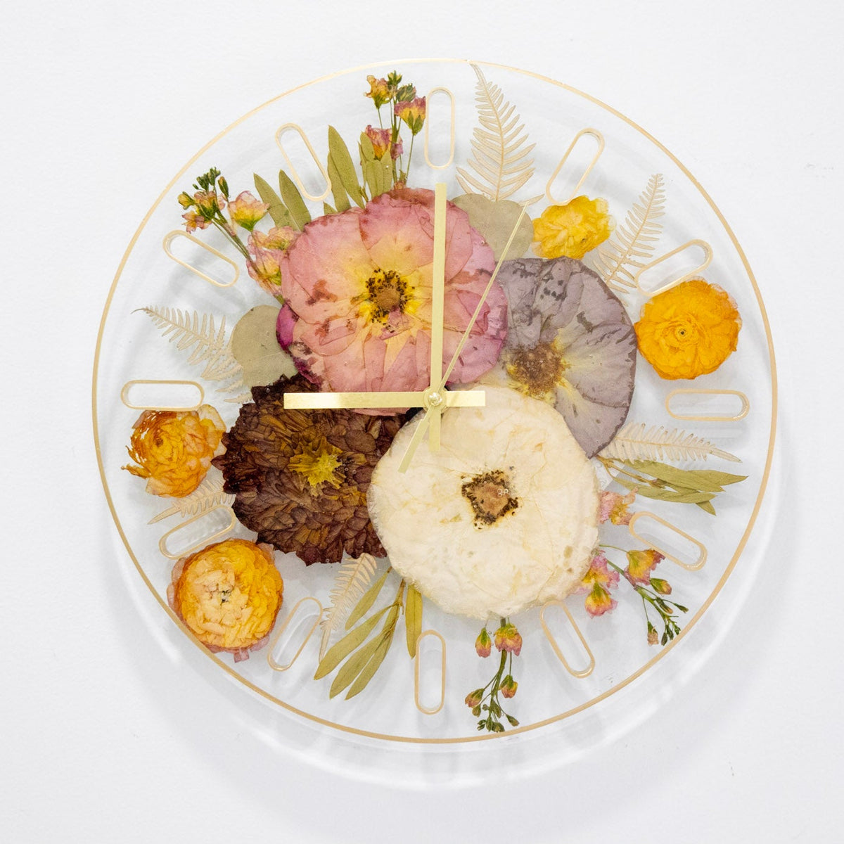 A top-down view of a resin flower preservation wall clock with a gold rim, featuring dried flowers and botanical elements arranged around gold clock hands.