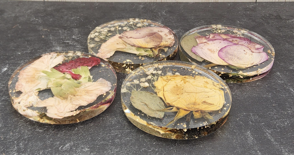 Set of four round resin coasters with embedded dried flowers on a dark surface