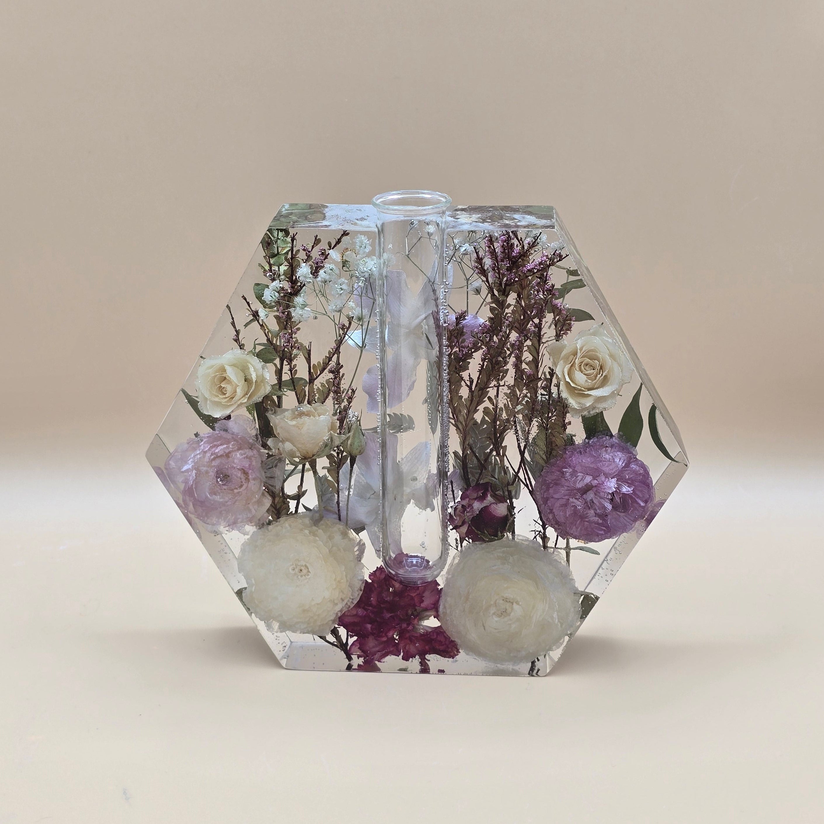 Hexagonal resin vase with embedded flowers and greenery on a beige background
