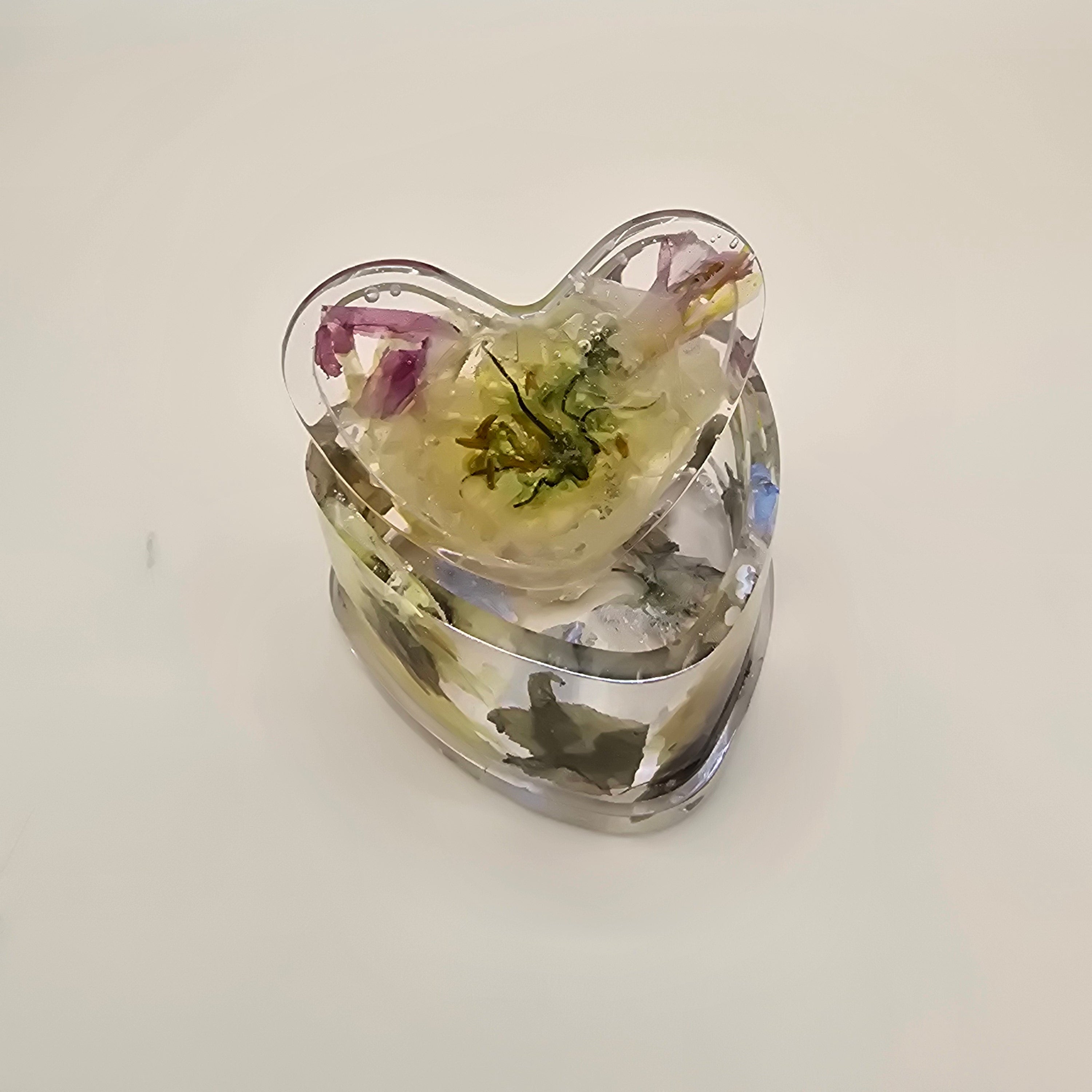 Heart-shaped resin jewelry box with embedded green and purple petals on a light background