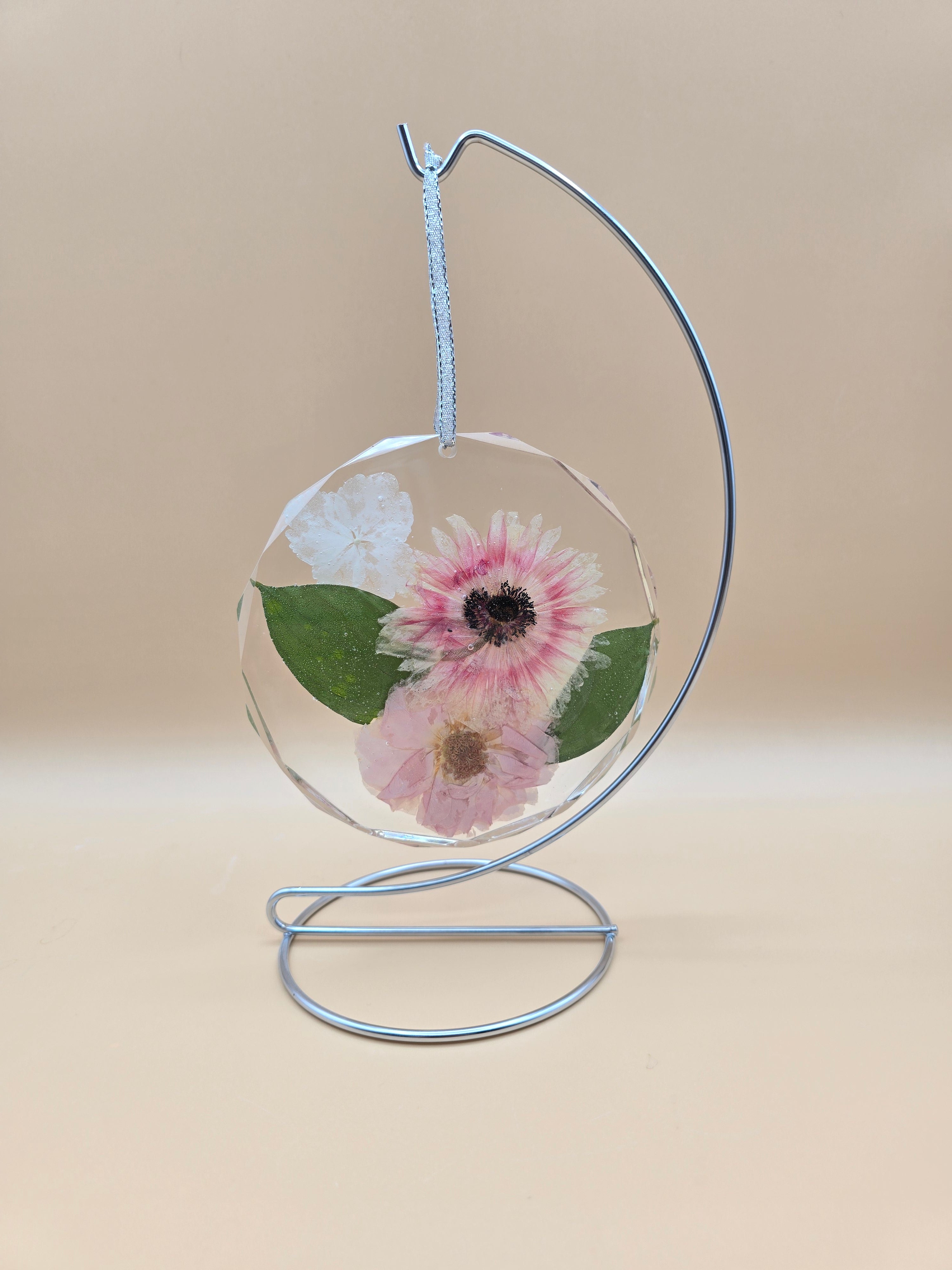 Preserved flowers in a clear resin circle ornament on a silver ribbon and stand